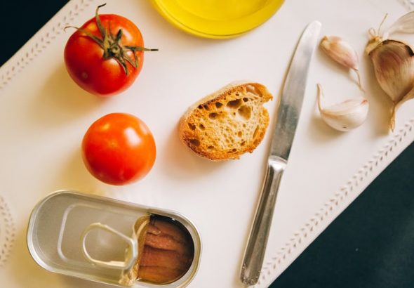 Tomatoes, bread, and sardines arranged for Catalán toast preparation.