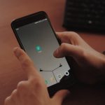 Hands interacting with smartphone on a wooden desk, highlighting modern technology.