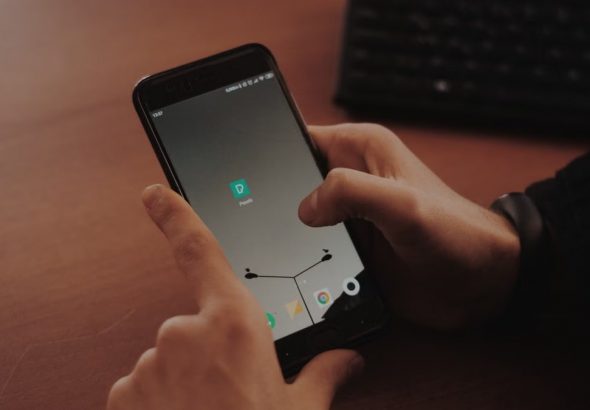 Hands interacting with smartphone on a wooden desk, highlighting modern technology.