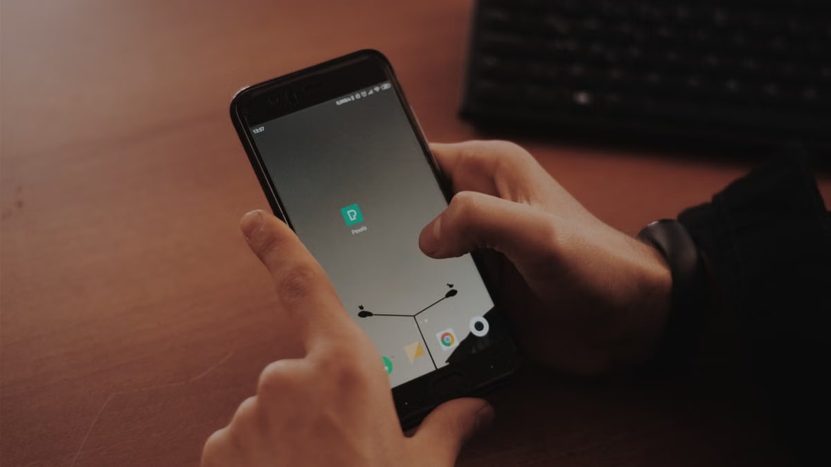 Hands interacting with smartphone on a wooden desk, highlighting modern technology.